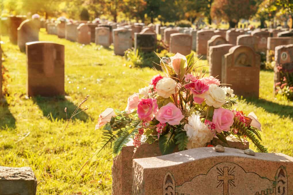 Cemetery at sunset with a pink and white rose arrangement on a gravestone